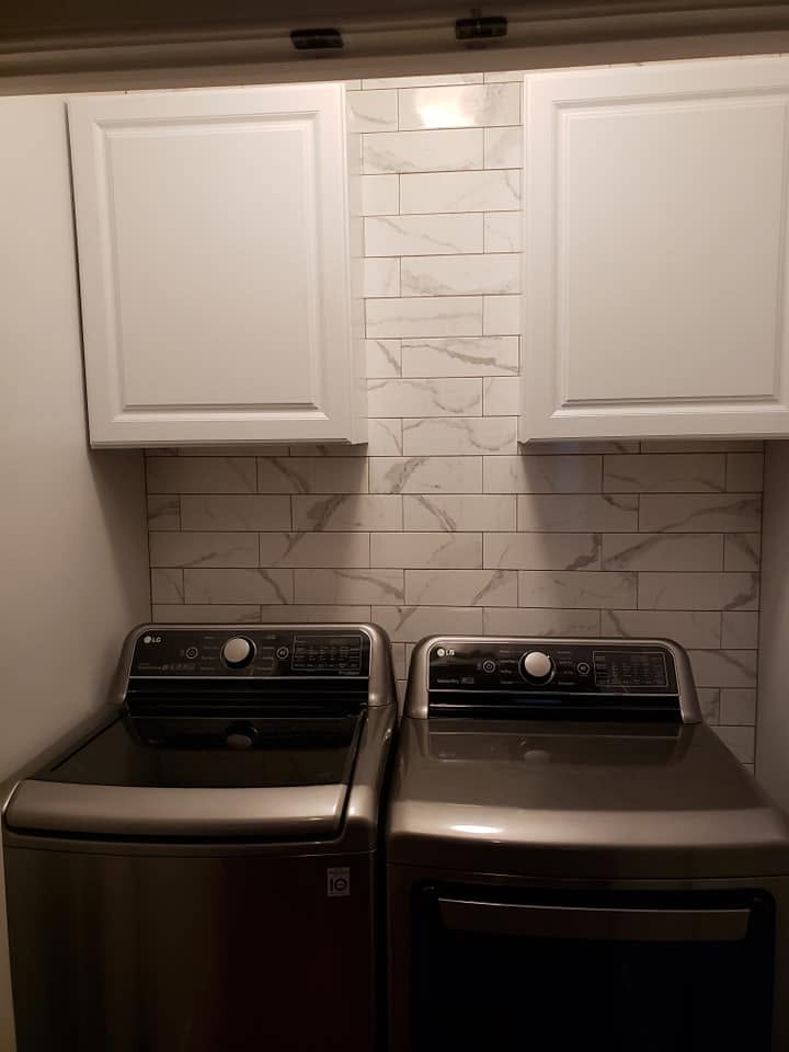 After: the same laundry closet with marble-look tile, white wall cabinets, and a new washer and dryer