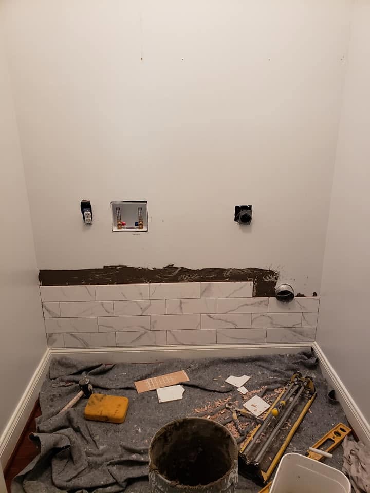 Before: laundry closet with bare walls, exposed hookups, and the first row of tile