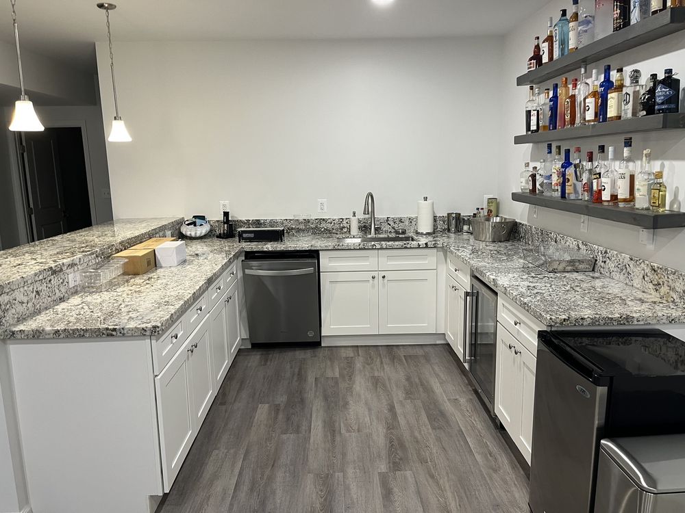 Finished wet bar with white cabinets, granite, and a gray floor