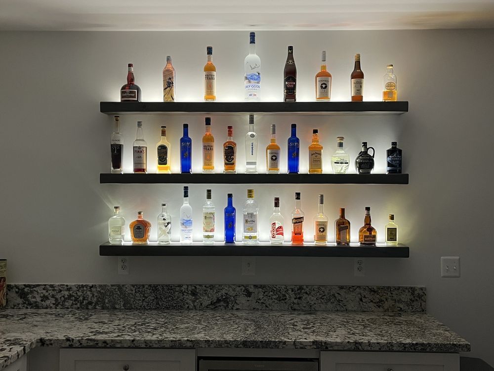 Three backlit shelves of bottles over a granite counter